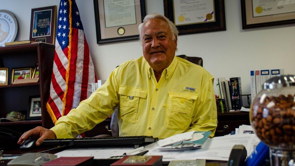 Lauren "Bubba" McDonald Jr. is shown sitting at his desk with a US flag in the background.