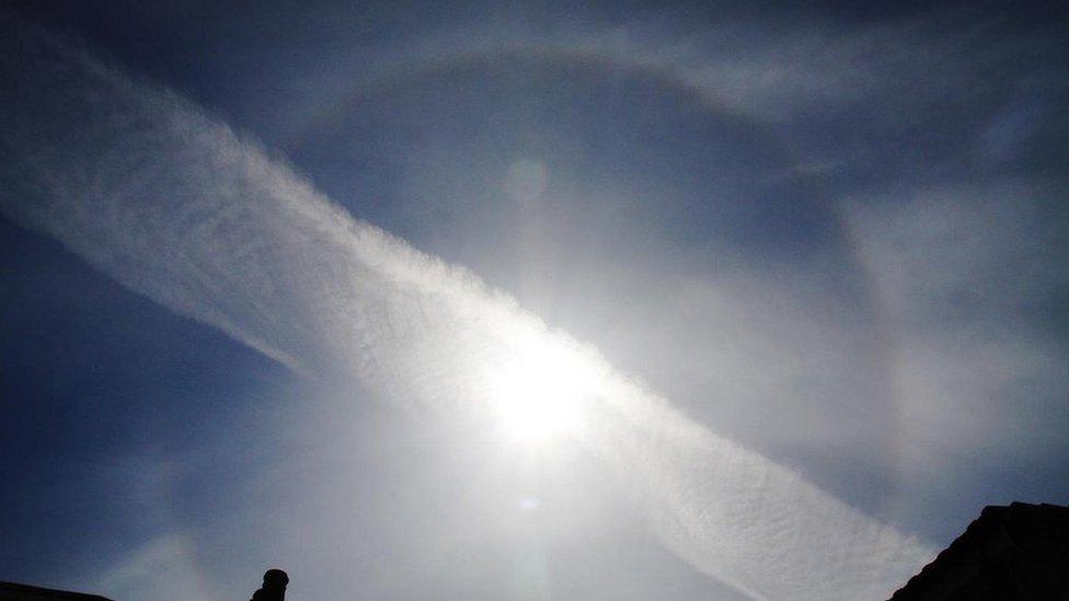 A ring around the sun. A plane contrail runs across it