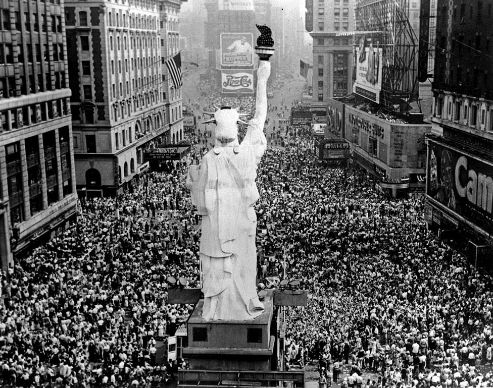 A scaled-down version of the Statue of Liberty is surrounded by cheering crowds