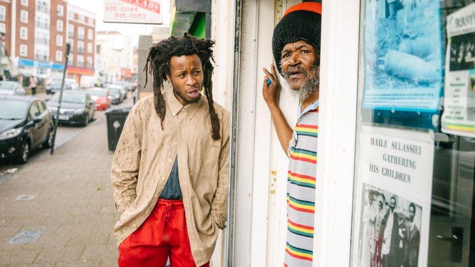 Mr Ogunmefun-Brooker leaning on a wall and Ras Bandele Selassie looking out of the door