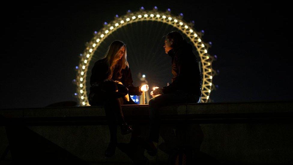 A couple sit on a wall opposite the London Eye with candles on March 23, 2021 in London, England.