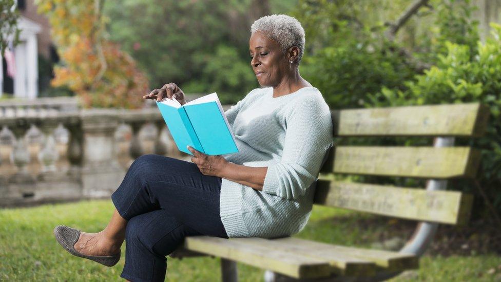 A woman sitting reading on a bench in a park