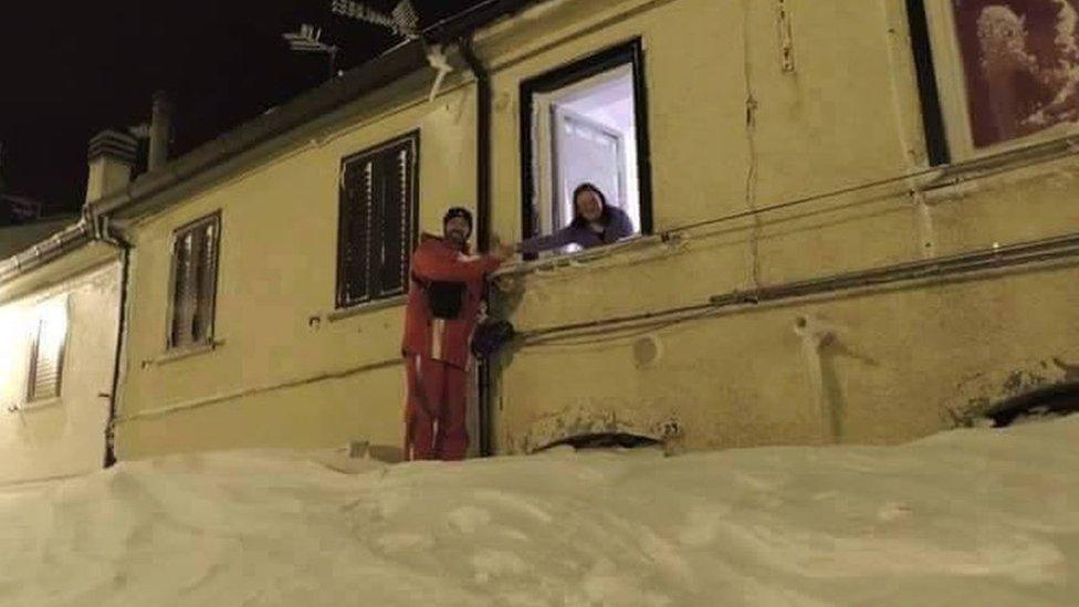 A man shakes hands with a woman, outside a window atop a mound of snow