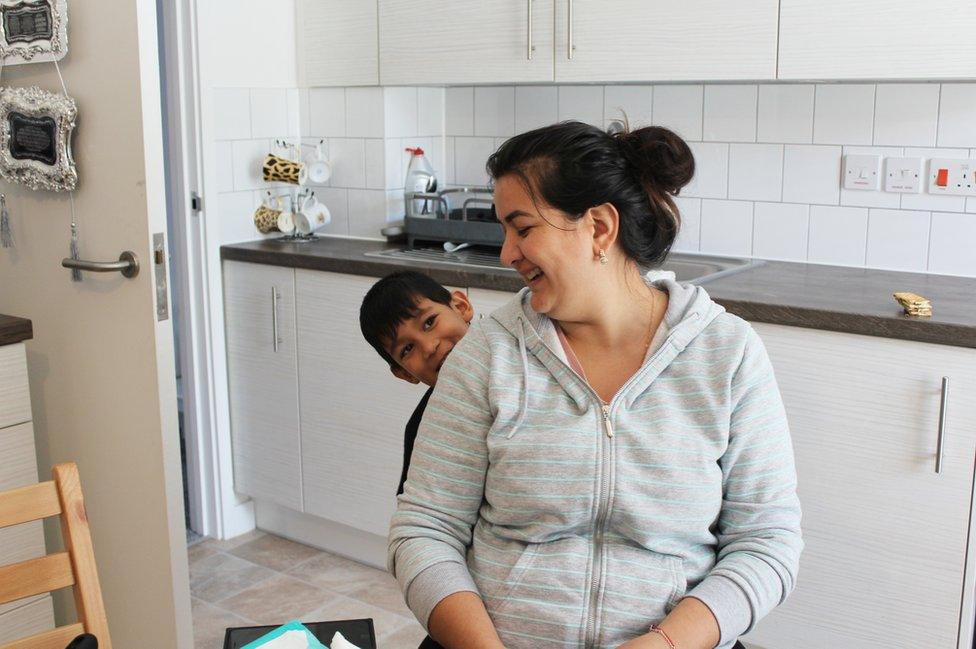 A young boy hides behind his mother