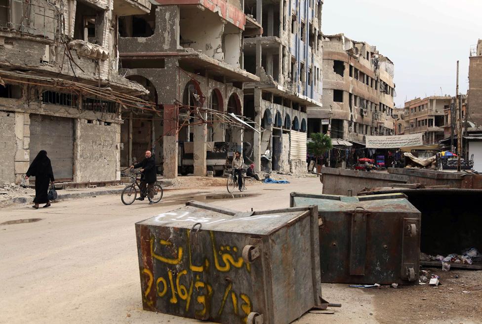 Syrians pass anti-election graffiti on a dust bin in the rebel-held city of Douma on the eastern outskirts of the capital on April 13, 2016.