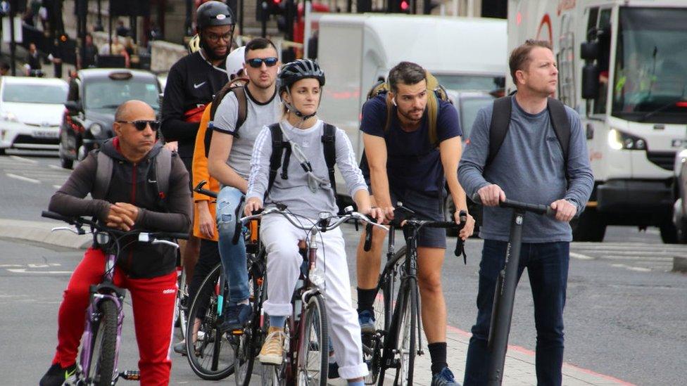 Cyclists and an electric scooter rider wait at traffic lights near Westminster Bridge