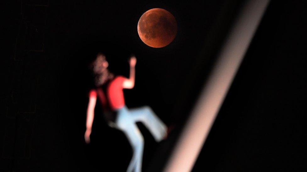 A 'blood moon' eclipse is pictured with a sculpture by the American artist Jonathan Borofsky 'Woman walking to the sky' on July 27, 2018 in Strasbourg, eastern France.