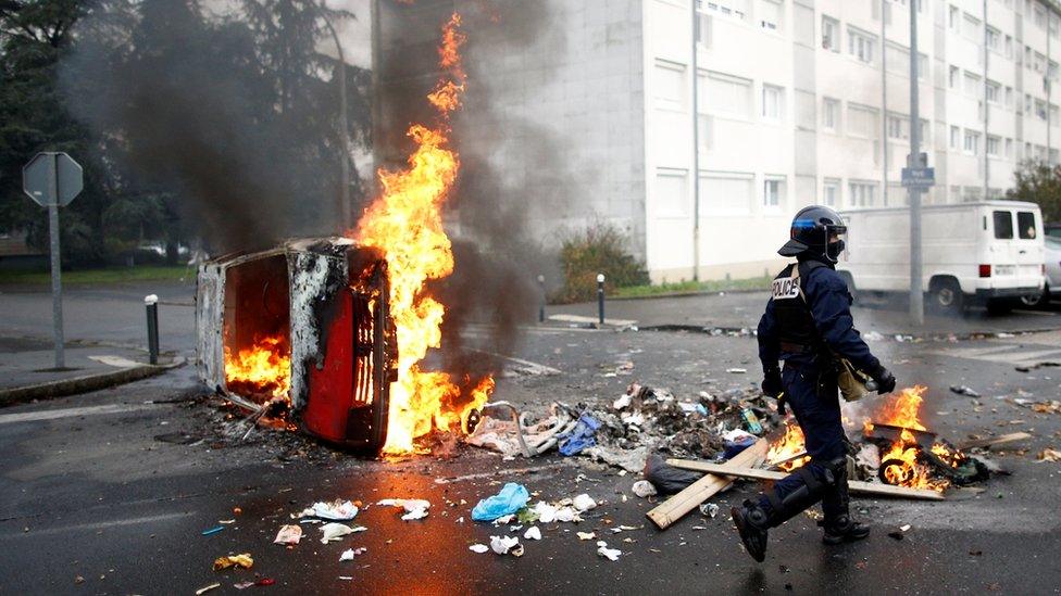 A French riot policeman walks past a burning car as youth and high school students protest against the French government's reform plan, in Nantes, France, December 6, 2018