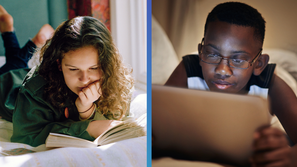 A young girl reads a paper book and a young boy reads on a tablet