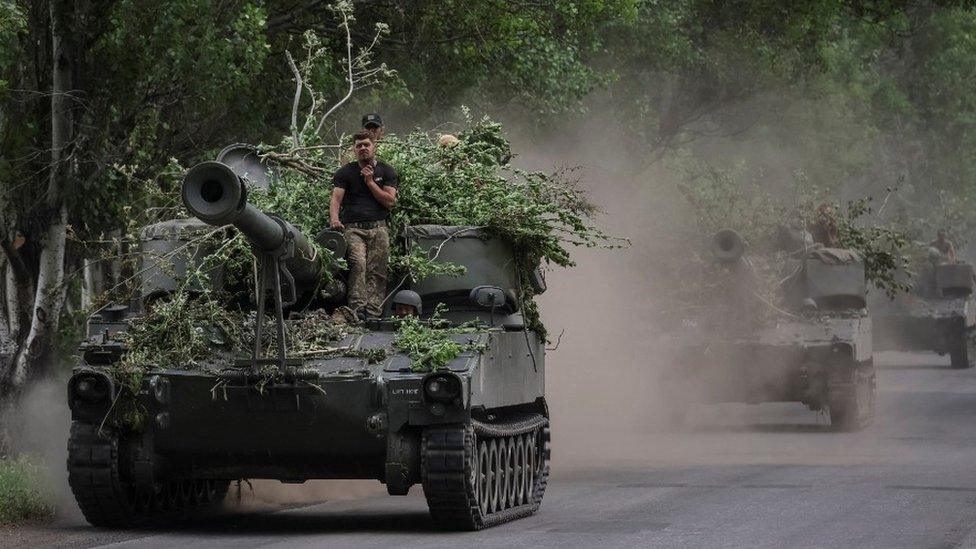 Ukrainian servicemen ride atop self-propelled guns