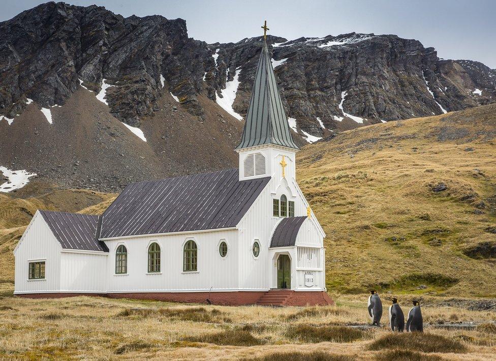 Three penguins looking at a church in the mountains