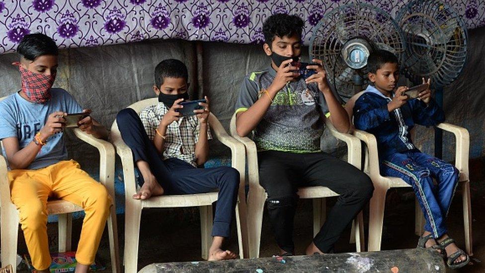 Children play games on their mobile phones at a street corner in Mumbai on September 6, 2021