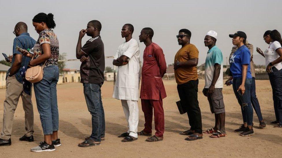 People in line to write their names on a unofficial voters list as they wait for election material to arrive at a polling station in Abuja on February 25, 2023, before polls open during Nigeria's presidential and general election