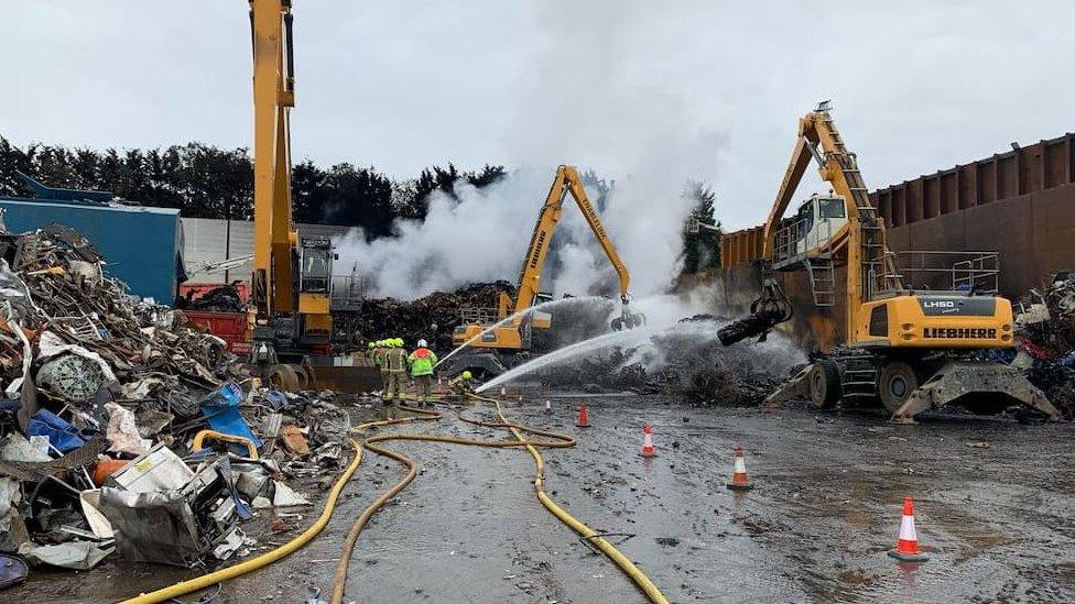 Firefighters putting out the fire with piles of scrap metal surrounding them