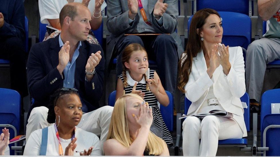 The Duke and Duchess of Cambridge either side of their daughter Princess Charlotte who is pulling a face