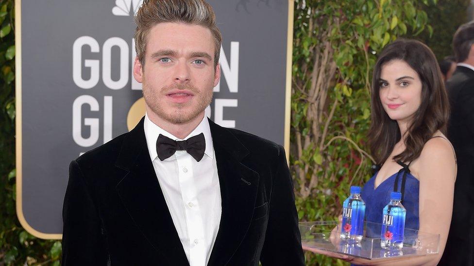 Model stands and poses in background of shot with actor Richard Madden