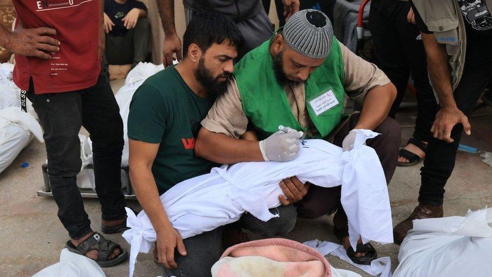 a man writes the name of a child on the shroud at al aqsa hospital in deir al balah