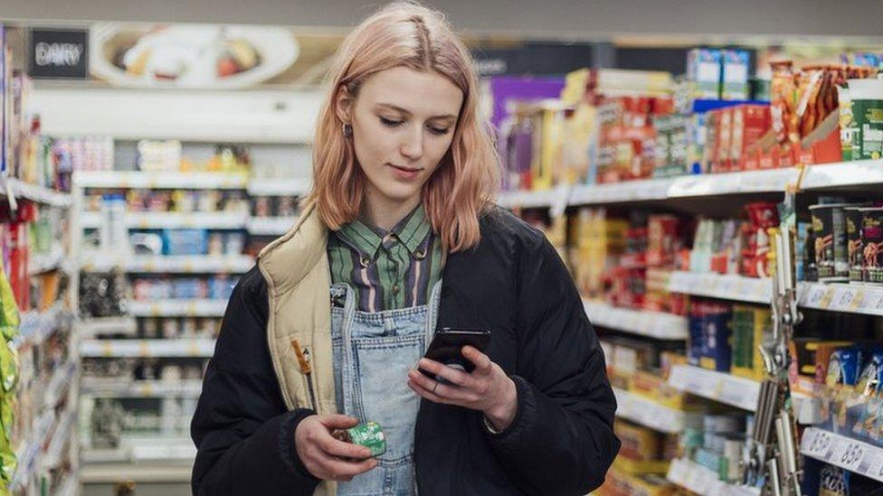 Woman looks at phone while holding a box of stock cubes in a grocery store