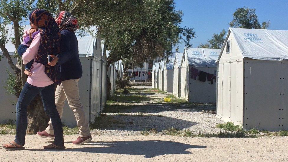 Migrant women walk in front of tents at a camp in Lesbos, Greece