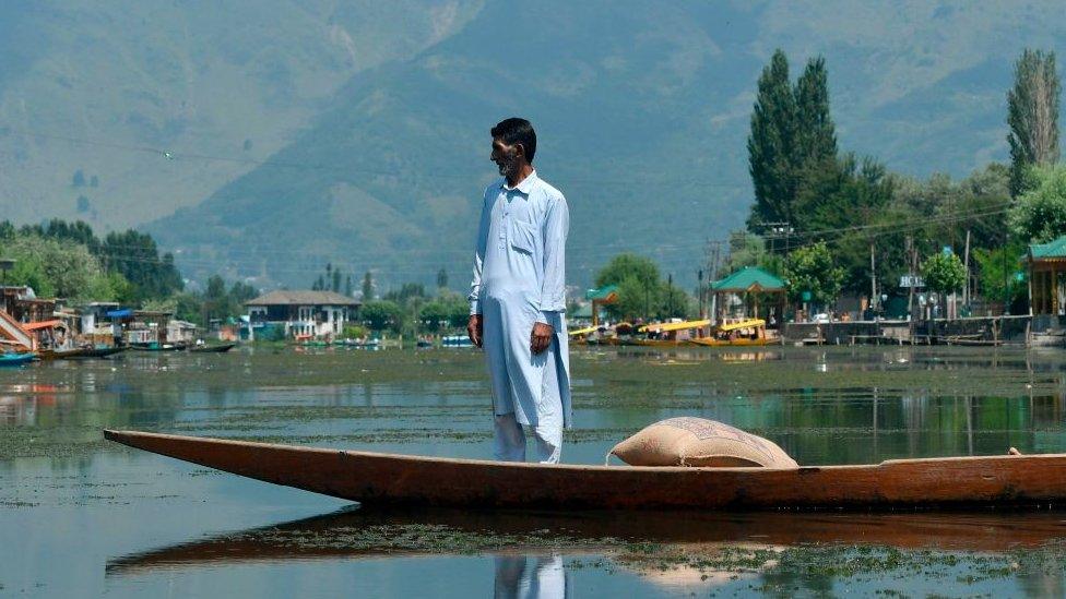 An Indian Kashmiri man stands in a traditional boat known as Shikara while travelling at Dal Lake in Srinagar on August 18, 2019