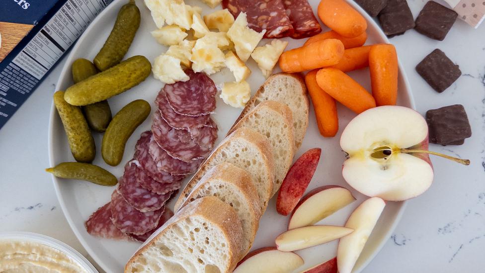 An example of "girl dinner"- a plate filled with pickles, cheese, bread, carrot and apple slices