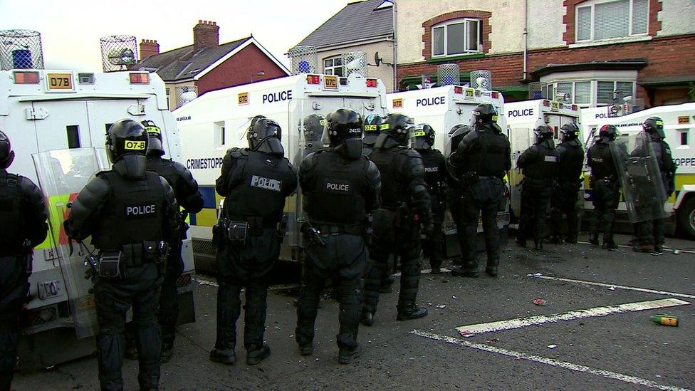 Police officers in riot gear standing behind police Land Rovers in north Belfast