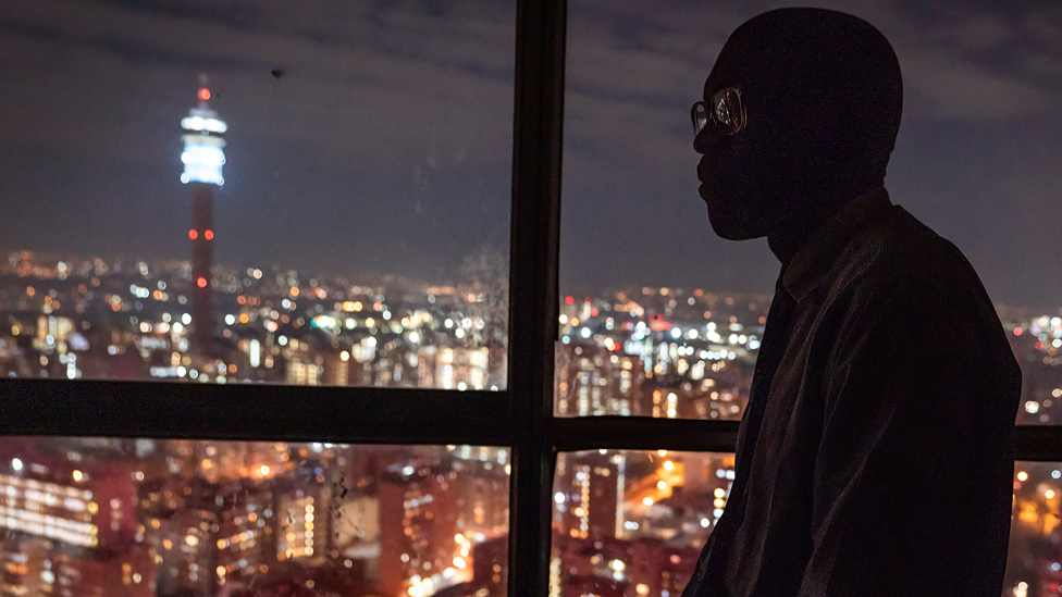 A man from DR Congo seen at a window with Hillbrow in the background - Johannesburg, South Africa