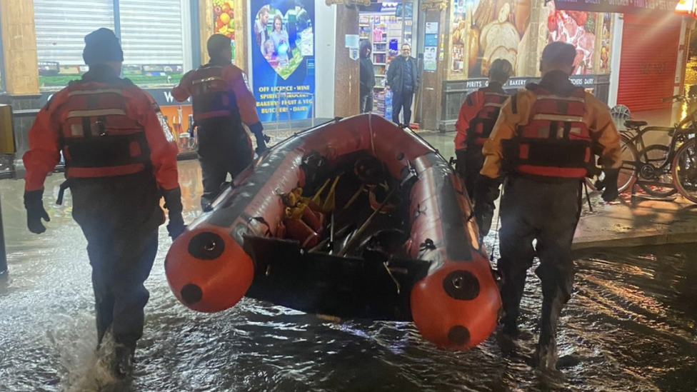 Firefighters carry a rescue dinghy through flood water in Blackheath