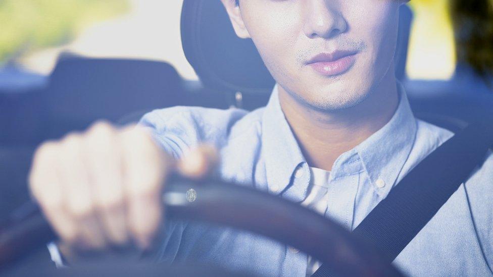 An driver with one hand on the steering wheel of his car