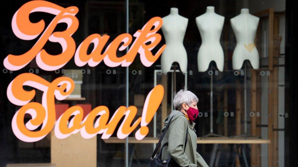 A woman wearing a Covid mask walking past a shop saying 'Back soon' in Cardiff