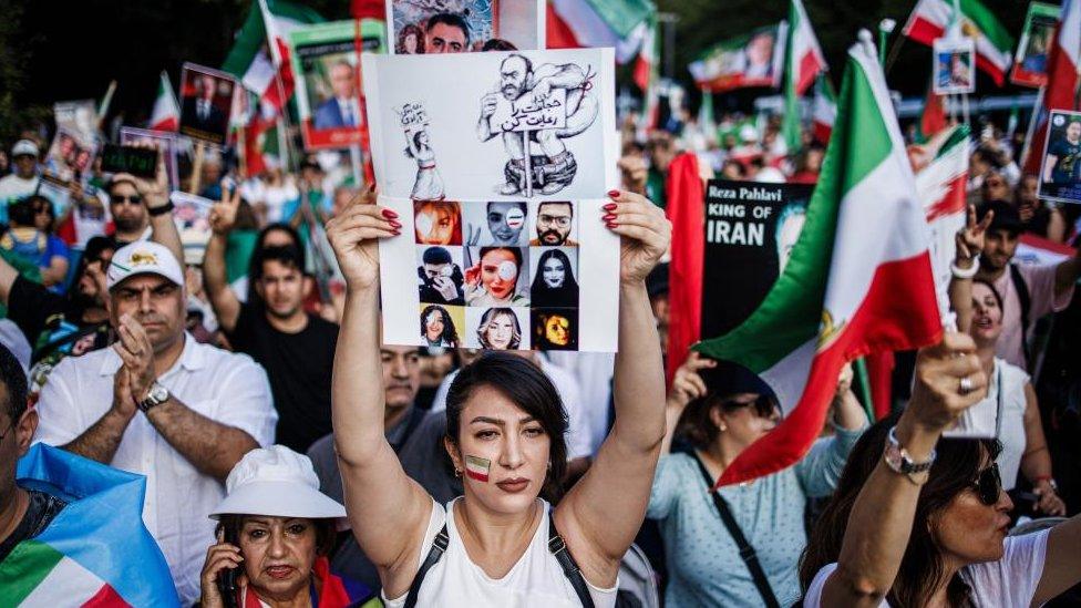 A woman with a flag painted on her cheek holds a sheet showing photos of victims during a rally in Berlin, Germany