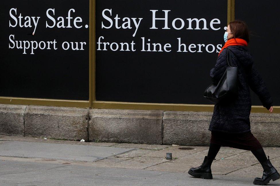 A woman walks past a shop hoarding which reads: "Stay safe. Stay home. Support our frontline heroes."