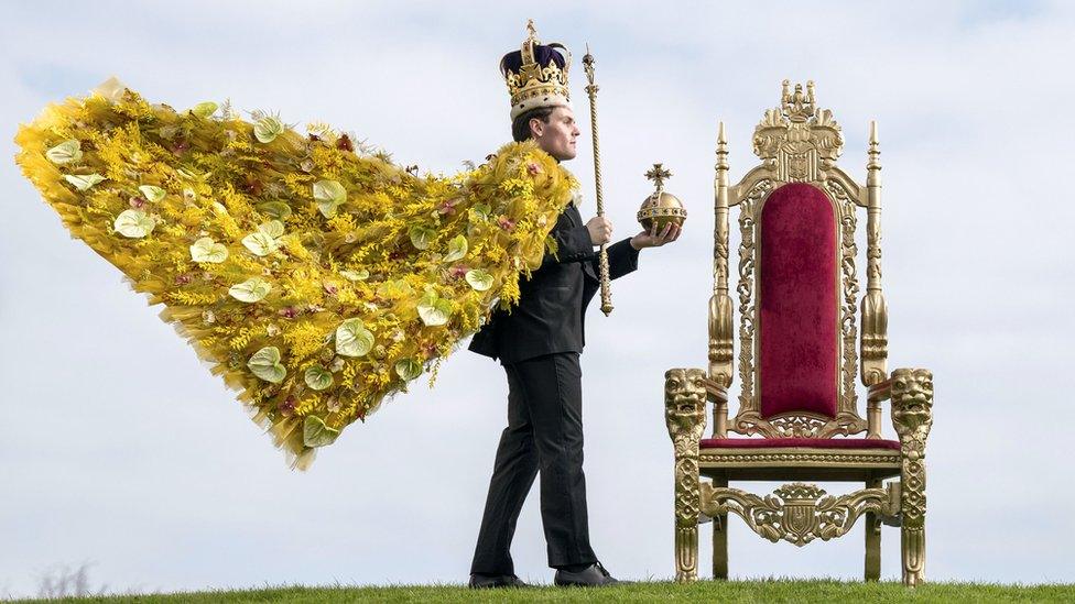 Model wearing robe made of flowers, a replica crown and holding a sceptre and orb