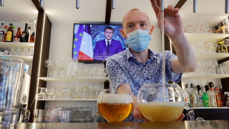 A man pours a beer in a bar while President Macron is on the TV behind him.