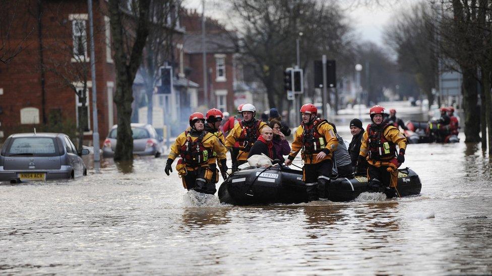 Lifeboat volunteers pull a dinghy with people onboard through flooded water in a residential street