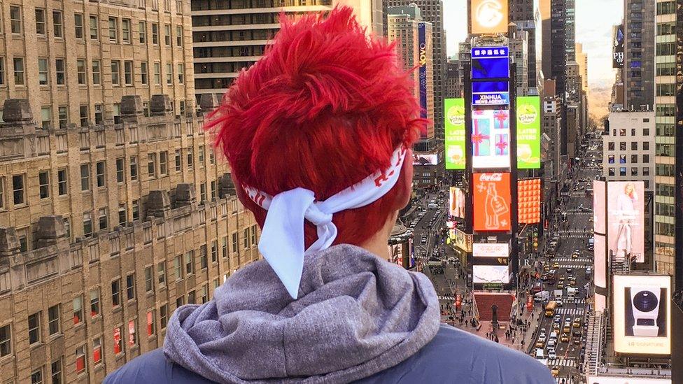 Ninja looks out over a skyscape of New York. His two trademarks are most visible - fluorescent, coloured hair and a bandana.