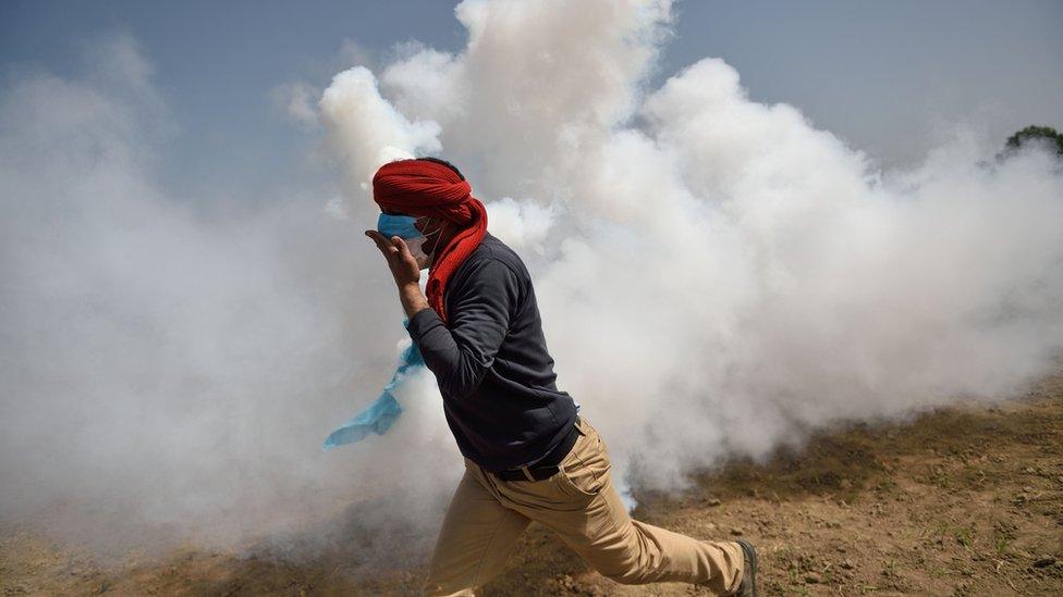 A man runs away from tear gas fired by Macedonia as migrants and refugees tried to break down the border fence near their makeshift camp at the Greek-Macedonian border in Idomeni (13 April 2016)