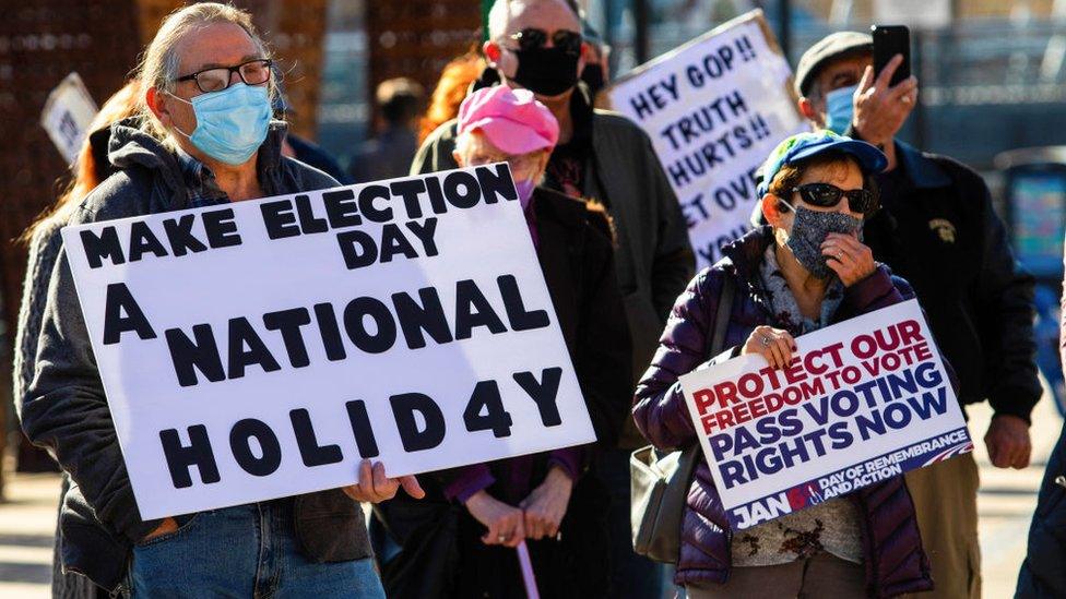 Protesters hold a sign reading 'make election day a national holiday'