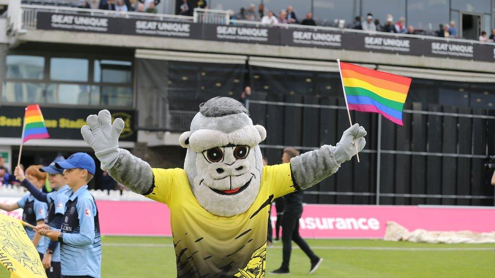 Gloucestershire County Cricket Club mascot holding LGBTQ+ flag