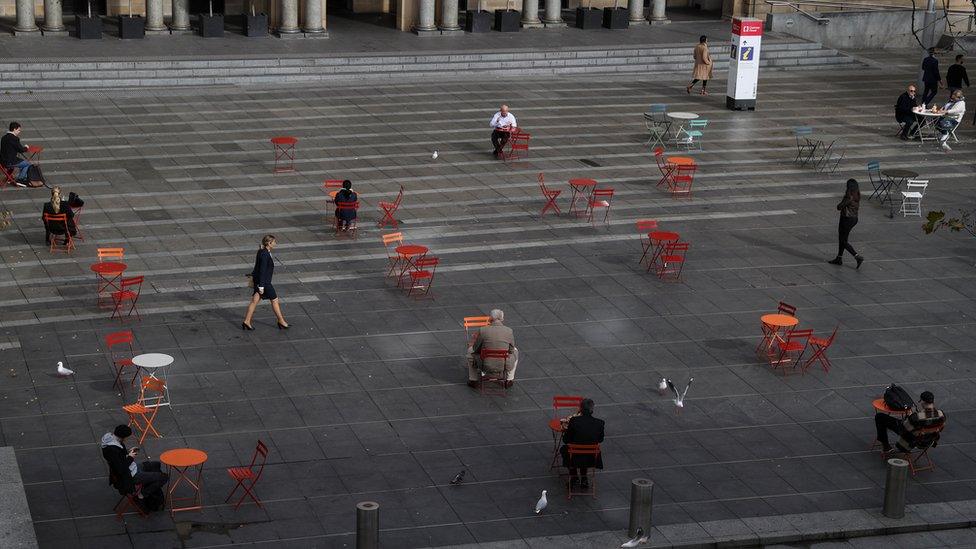 A few people sit at distanced tables in Martin Place in central Sydney