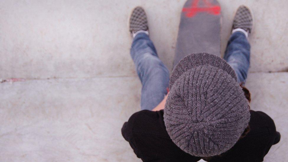 Boy with skateboard sat on steps, viewed from above