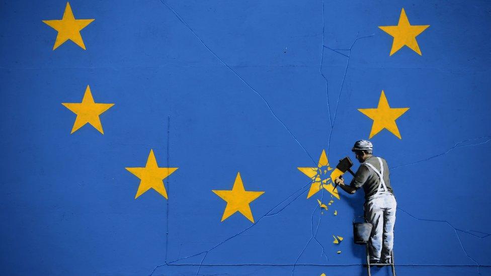 A picture of a mural depicting a workman chipping off one of the stars on an EU-themed flag