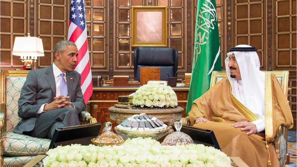 President Obama and King Salman sitting in front of their respective countries' flags, surrounded by white roses