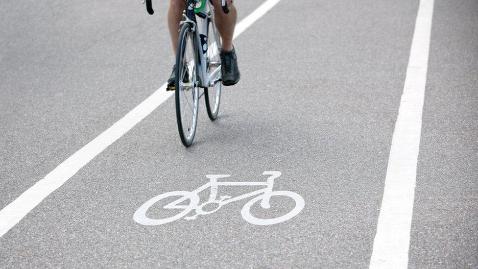 Commuter riding a bicycle on a city cycle lane or path across white painted bike symbol