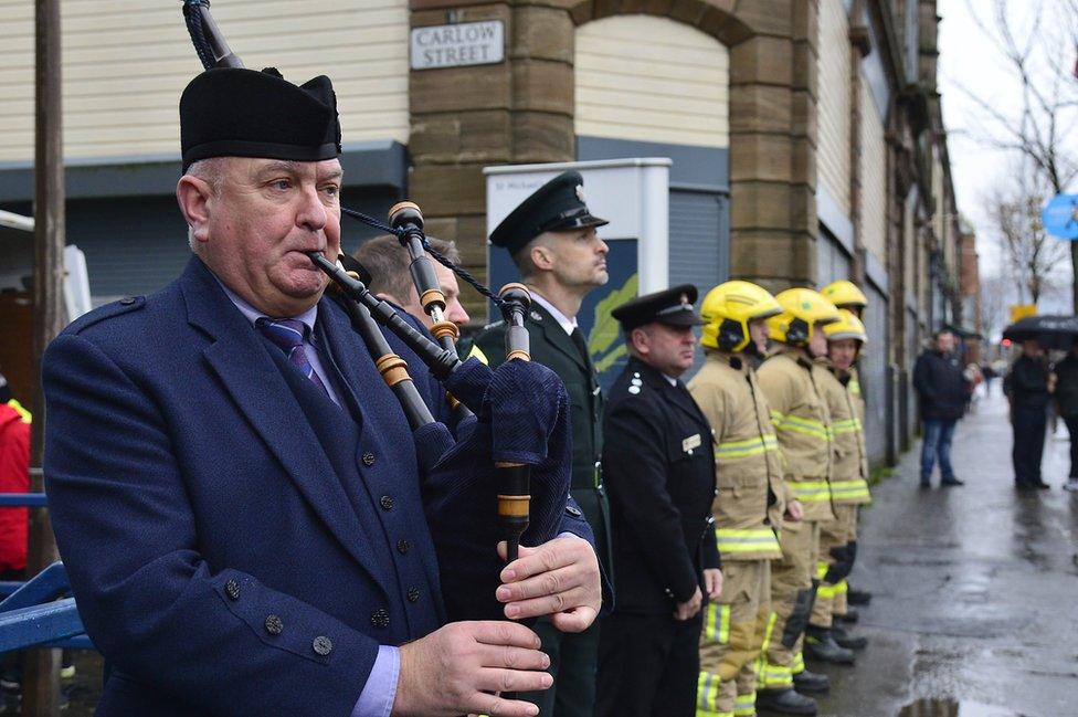 A piper plays as members of the emergency services stand at the service on Shankill Road