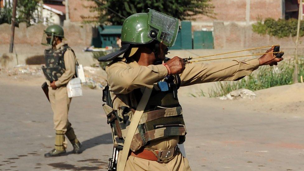 An Indian paramilitary officer aims a sling shot towards Kashmiri protestors during a clash in downtown Srinagar