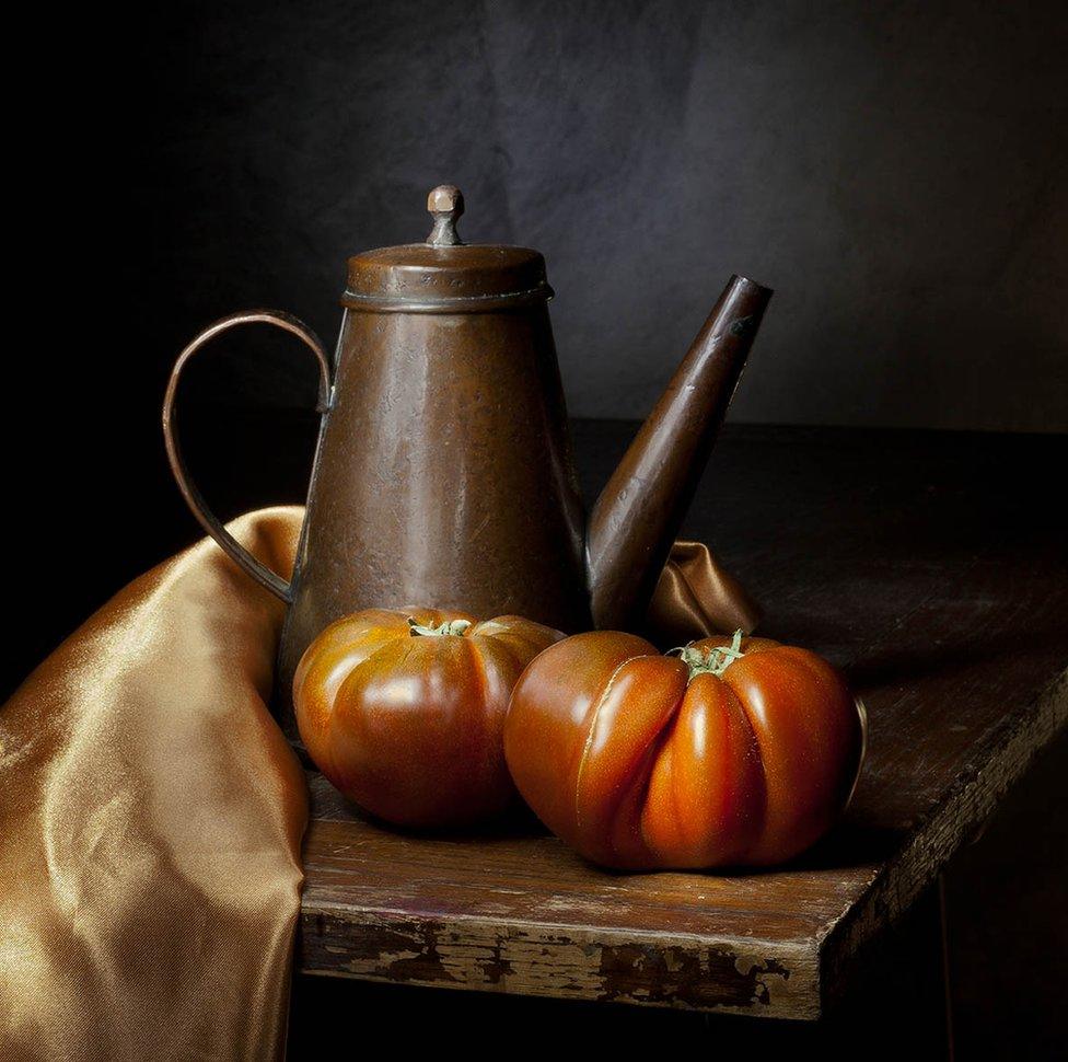 An old copper kettle on a table with large tomatoes