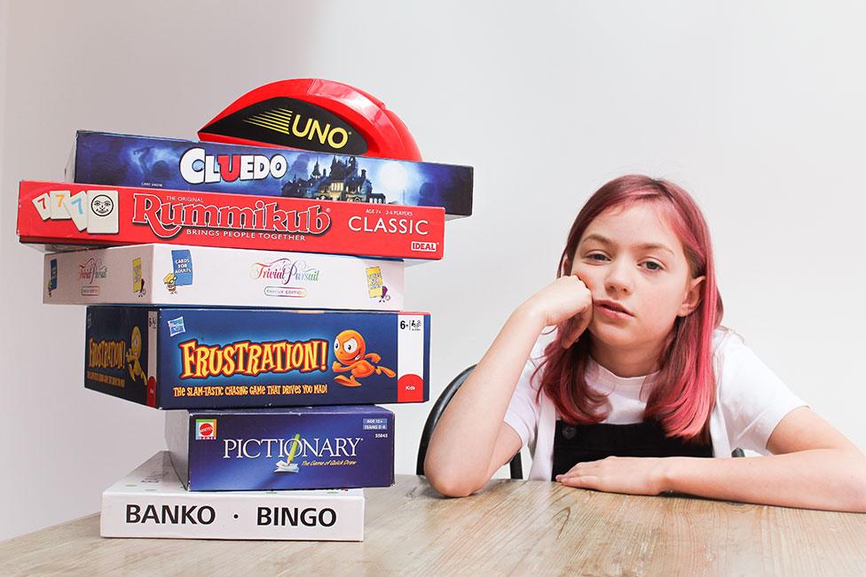 A girl looks bored next to a stacked pile of board games