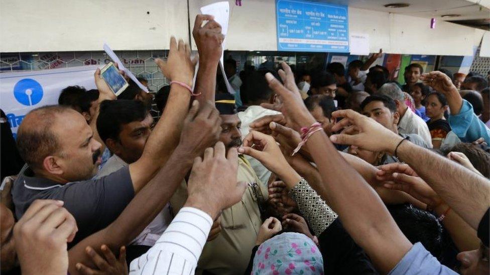 Indians stretch out their hands to collect withdrawal slips from a police officer to deposit and exchange discontinued currency notes outside the State bank of India in Mumbai, India, Thursday, Nov. 10, 2016.