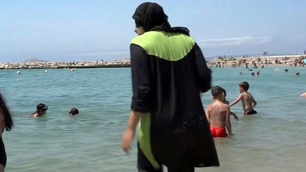 A woman wearing a full-body swimming costume walks into the water at a beach in France (file pic)